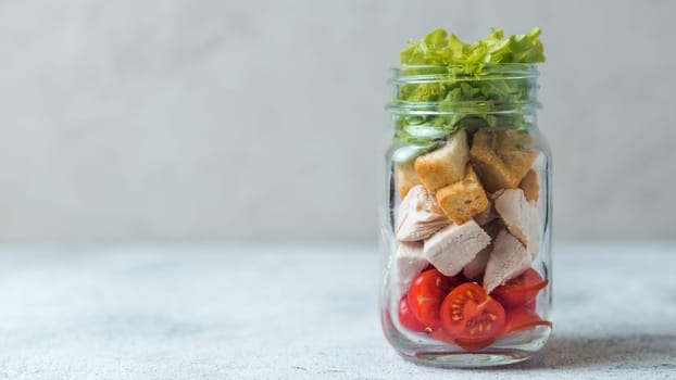 Caesar salad in glass mason jar on gray background. Copy space for text. Homemade healthy caesar salad layered in jar. Healthy food, trendy modern food, diet concept, idea, recipe.