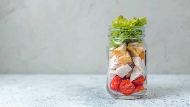 Caesar salad in glass mason jar on gray background. Copy space for text. Homemade healthy caesar salad layered in jar. Healthy food, trendy modern food, diet concept, idea, recipe.