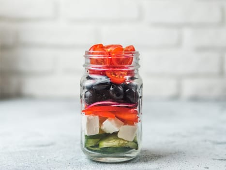 Greek Salad layered in glass mason jar on gray background, copy space. Trendy food. Idea, recept and concept of modern healthy food.