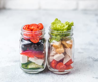 Greek Salad and Caesar salad in glass mason jar on gray background.Homemade healthy caesar salad and greek salad layered in jars.Healthy food, trendy modern food, diet concept, idea, recipe.Copy space