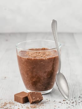 Chocolate chia pudding in glass and chocolate cubes slice on gray wooden table. Healthy vegan breakfast with copy space.