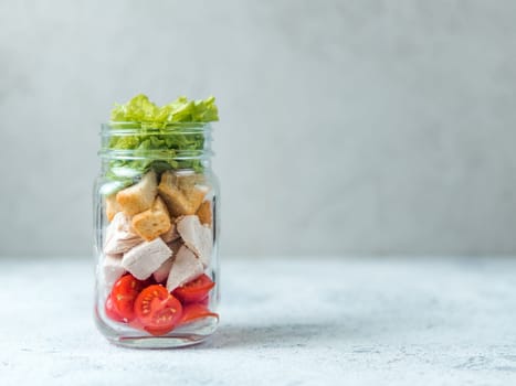 Caesar salad in glass mason jar on gray background. Copy space for text. Homemade healthy caesar salad layered in jar. Healthy food, trendy modern food, diet concept, idea, recipe.