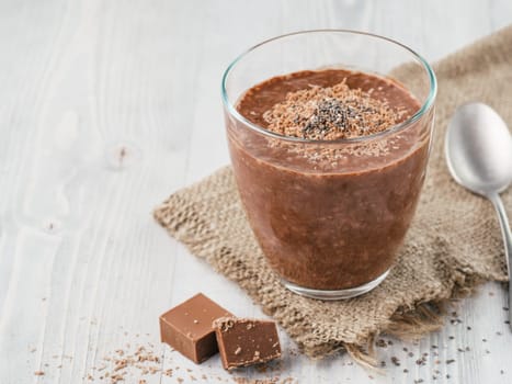 Chocolate chia pudding in glass and chocolate cubes slice with rustic napkin on gray wooden table. Healthy vegan breakfast with copy space.