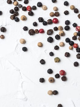Assorted peppercorns. Medley trio colorful peppercorn on white textured concrete background with copy space. Top view or flat lay. Vertical