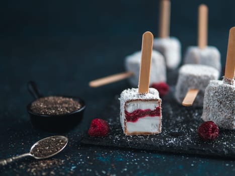 Homemade raw lamington ice cream pops on dark background. Australian sweet dessert lamington with chia and raspberries jam, chocolate and cocoa coat. Vegan food recipe and idea. Copy space for text