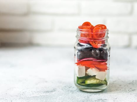 Greek Salad layered in glass mason jar on gray background, copy space. Trendy food. Idea, recept and concept of modern healthy food.