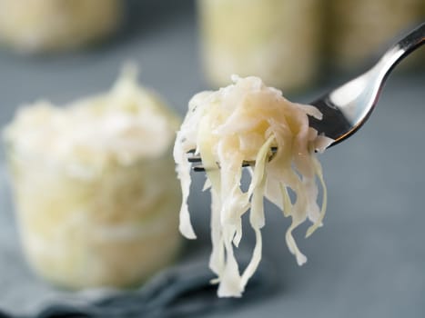 Sauerkraut on fork and unfocused glass jars with kraut. Pickling or fermented cabbage at table in home. Homemade sauerkraut with copy space for text