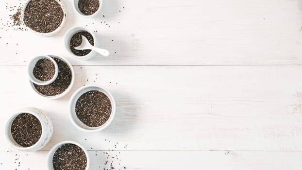 Organic chia seeds on white wooden table. Set of small bowls with organic chia seed. Superfood concept. Copy space. Top view or flat-lay. Banner