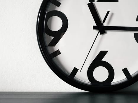 Modern minimalistic clock or simple white and black on black wooden table and white wall with space for text