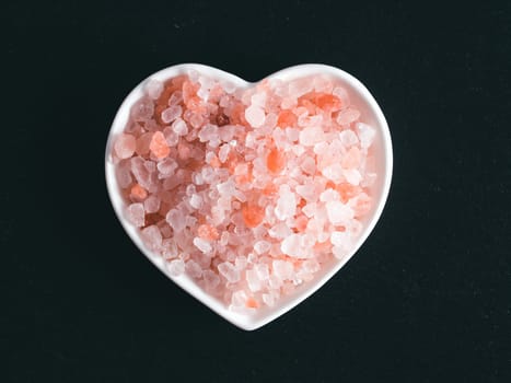 Himalayan pink salt in hearth-shape bowl on black stone background. Copy space