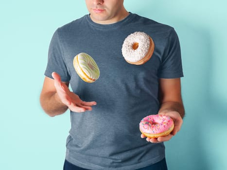 Juggler man juggles donuts on blue background. Doughnuts delivery or unhealthy diet concept. Flying glazed donuts with sprinkles and desiccated coconut in male hands