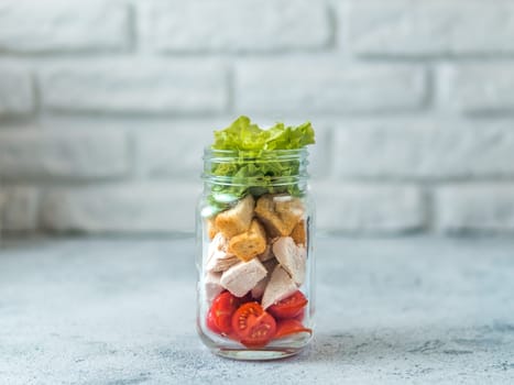 Caesar salad in glass mason jar on gray background. Copy space for text. Homemade healthy caesar salad layered in jar. Healthy food, trendy modern food, diet concept, idea, recipe.