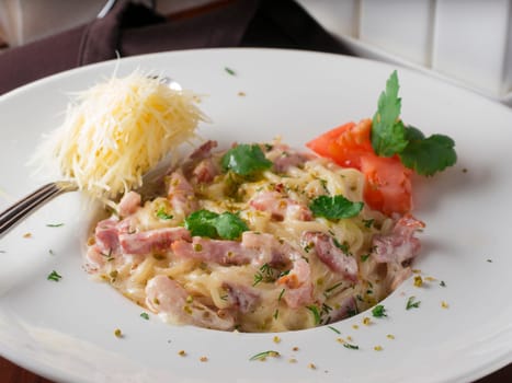 pasta carbonara on white plate with grated cheese in spoon close-up on dark brown wooden table in restaurant