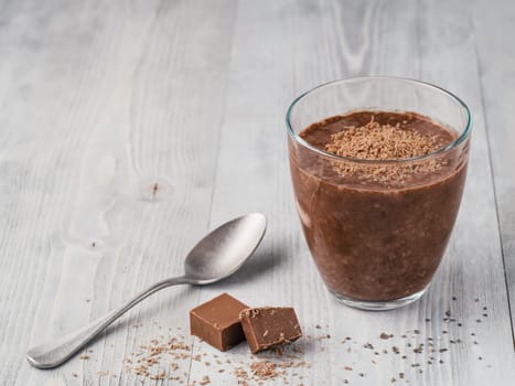 Chocolate chia pudding in glass and chocolate cubes slice on gray wooden table. Healthy vegan breakfast with copy space.