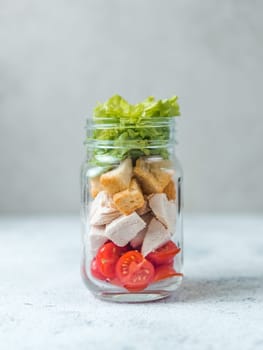 Caesar salad in glass mason jar on gray background. Copy space for text. Homemade healthy caesar salad layered in jar. Healthy food, trendy modern food, diet concept, idea, recipe. Vertical.
