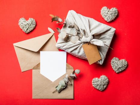 Zero waste Valentine's Day concept and mock up on red. Eco-friendly gift cloth wrapping in Furoshiki style, craft paper envelope,empty greetings card. Top down view or flat lay. Copy space for design