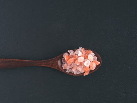 Himalayan pink salt in spoon on black stone background. Copy space