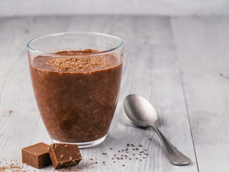 Chocolate chia pudding in glass and chocolate cubes slice on gray wooden table. Healthy vegan breakfast with copy space.