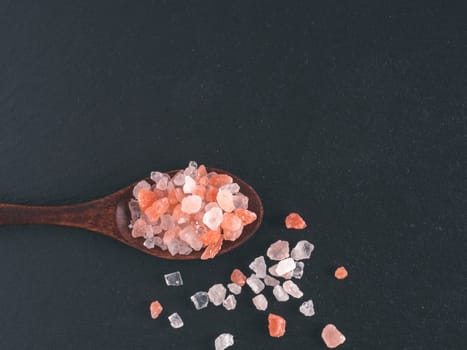 Himalayan pink salt in spoon on black stone background. Copy space