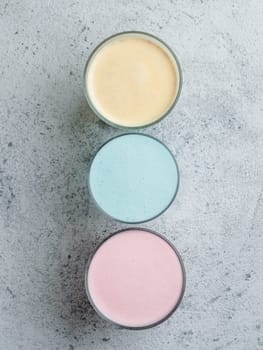 Trendy drinks: Blue, yellow and pink latte. Top view of hot butterfly pea or blue spirulina latte, yellow or gold turmeric latte and pink beetroot latte on gray cement background. Copy space for text