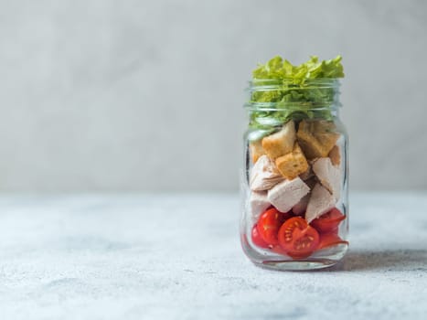 Caesar salad in glass mason jar on gray background. Copy space for text. Homemade healthy caesar salad layered in jar. Healthy food, trendy modern food, diet concept, idea, recipe.