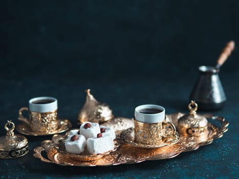 Turkish coffee with delight and traditional copper serving set on dark background. Assorted traditional turkish dilight or lokum and turkish coffee in metal traditional cups.Copy space.Selective focus