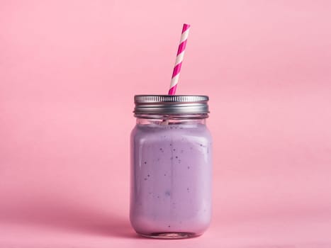 Blueberry smoothie in mason jar glass on pink background