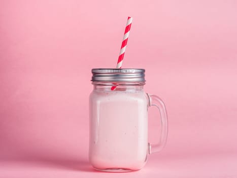 Pink strawberry smoothie in mason jar glass on pink background