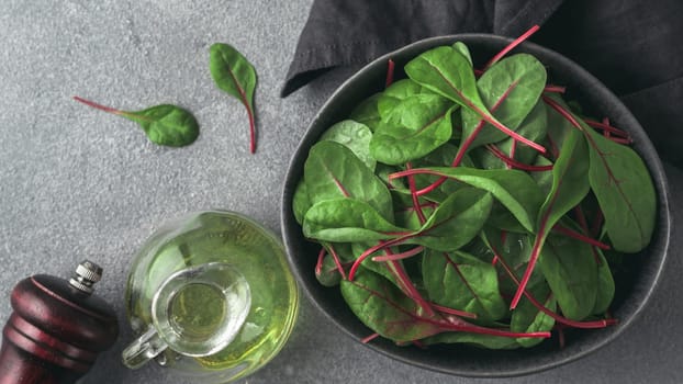 Fresh salad of green chard leaves or mangold on gray stone background. Flat lay or top view fresh baby beet leaves in craft ceramic bowl. Banner for web