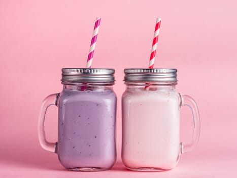 Strawberry and blueberry smoothie in mason jar glass on pink background.