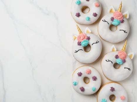 Unicorn donuts over white marble background. Trendy donut unicorn with white glaze. Top view or flat lay. Copy space for text.