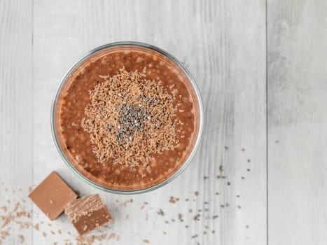 Chocolate chia pudding in glass and chocolate cubes slice on gray wooden table. Healthy vegan breakfast with copy space. Top view or flat-lay.