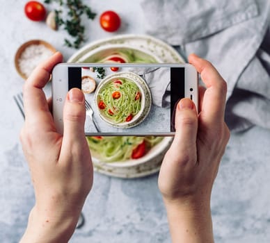 Woman hands takes top view photography of zucchini noodles salad on table with phone. Smartphone photo for social networks or blogging post.Vegetarian, healthy, organic, clean eating, raw food concept
