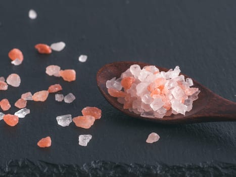 Himalayan pink salt in spoon on black stone background. Copy space