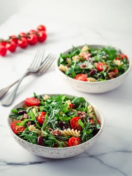 Warm salad with tuna, arugula, tomatoes ,red bean, pasta.Idea and recipe for healthy lunch or dinner.Two bowls with warm salads on marble table. Ideas and recipes for healthy dinner or lunch. Vertical