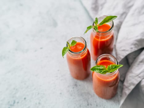 Delicious gaspacho soup in glass bottles. Traditional spanish cold soup puree gaspacho or gazpacho on gray cement background with copy space for text. View from above or top view or flat lay