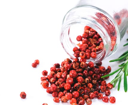 Dried pink pepper berries poured from glass jar on white wooden cutting board. Close up view of pink peppercorn and fresh rosemary on vintage wooden table. Copy space.