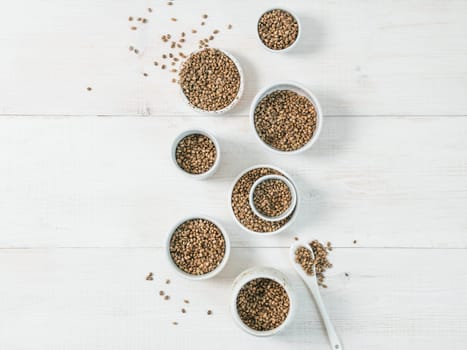 Hemp seeds in small white bowls and spoon on white wooden table. Set of small bowls with raw organic unrefined hemp seed. Superfood and vegan concept. Top view or flat lay.Copy space for text