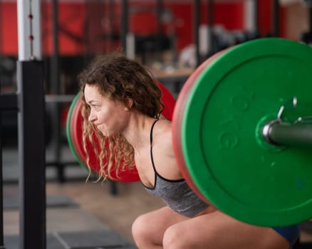 Middle-aged woman doing squats with a barbell in the gym