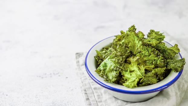 Green Kale Chips with salt on plate. Homemade healthy snack for low carb, keto, low calorie diet. Gray cement background. Ready-to-eat kale chips, copy space for text. Banner