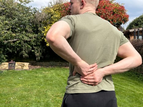 Rear view shot of a man holding onto his aching lower back outdoors