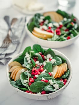 Vegan salad bowl with spinach, pear, pomegranate, cheese on marble tabletop. Vegan breakfast, vegetarian food, diet concept. Vertical