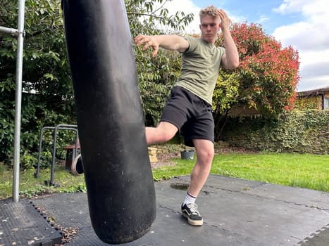 Young man working out in his garden, kicking punching bag