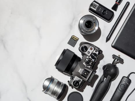 Photographer workplace with dslr camera, lens, pen tablet and camera accessorieson white marble background. Camera, photography, visual content concept. Flat lay or top view. Copy space. Hard light.