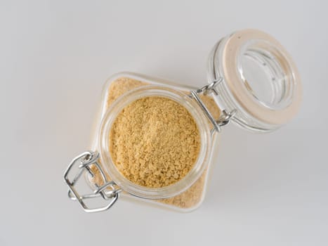 Nutritional yeast background. Nutritional inactive yeast in glass jar on white background. Copy space. Top view. Nutritional yeast is vegetarian superfood with cheese flavor, for healthy diet