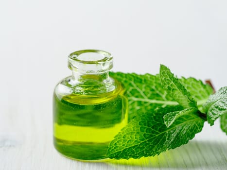 Organic essential mint oil or melissa oil with green leaves of mint. Mint melissa oil on white wooden tabletop