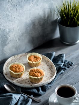 Homemade muffins on craft plate and coffee cup over gray wooden table. Carrot cupcakes with copy space. Toned image in scandinavian style.