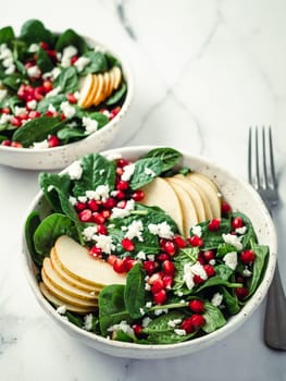 Fresh salad with baby spinach, pear, pomegranate and cottage cheese. Two bowls with delicious summer fruit salad on marble table. Copy space for text. Ideas and recipes for healthy breakfast or lunch