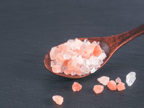 Himalayan pink salt in spoon on black stone background. Copy space