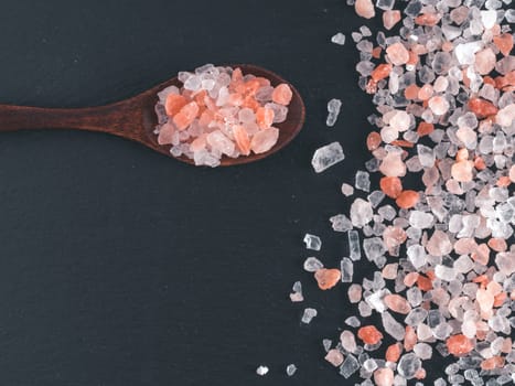 Himalayan pink salt in spoon on black stone background. Copy space